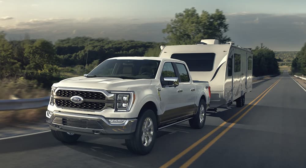 A white 2023 Ford F-150 is shown towing a trailer on an open road.