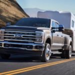 A grey 2023 Ford F-350 Super Duty is shown from the front at an angle while towing a camper.