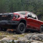 A red 2023 GMC Sierra 1500 AT4X is shown from the side parked on rocky terrain.