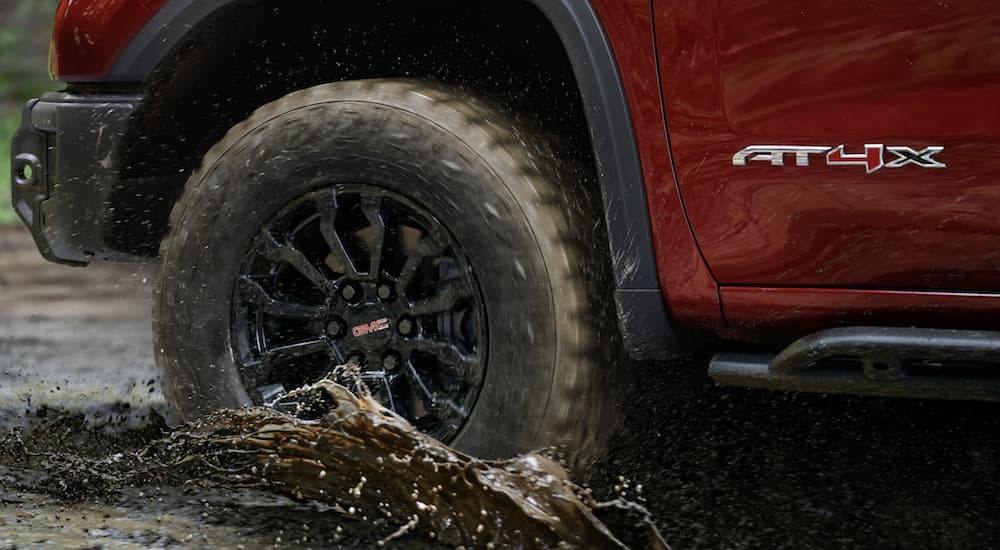 The tire of a 2023 GMC Sierra 1500 AT4X is shown driving through a river.