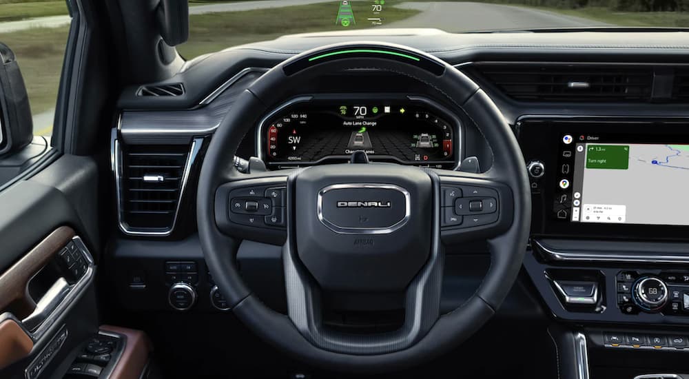 The black interior of a 2023 GMC Sierra 1500 Denali Ultimate shows the steering wheel and infotainment screen.