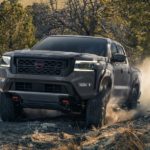 A grey 2023 Nissan Frontier is shown from the front driving on a dirt road.