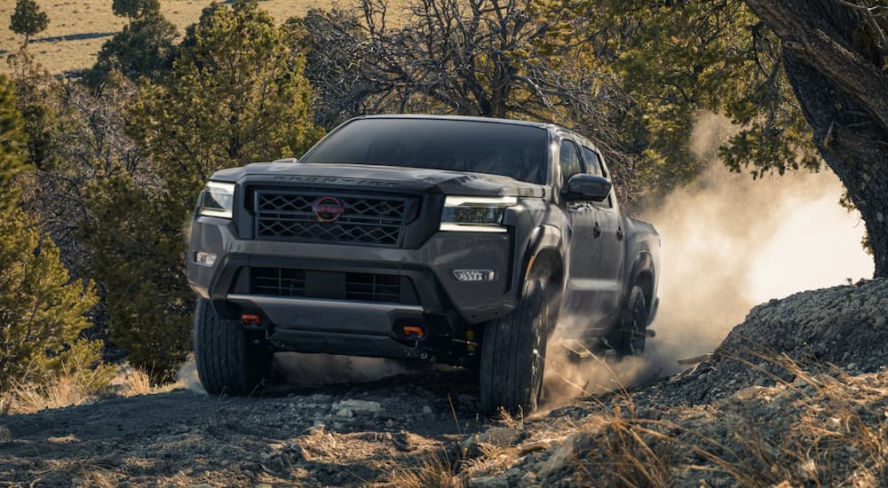 A grey 2023 Nissan Frontier is shown from the front driving on a dirt road.