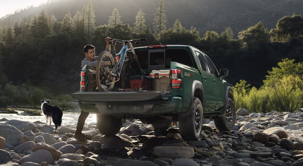 A green 2023 Nissan Frontier is shown from the rear parked near a river.