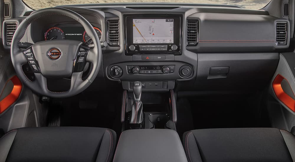 The grey interior of a 2023 Nissan Frontier shows the steering wheel and infotainment screen.