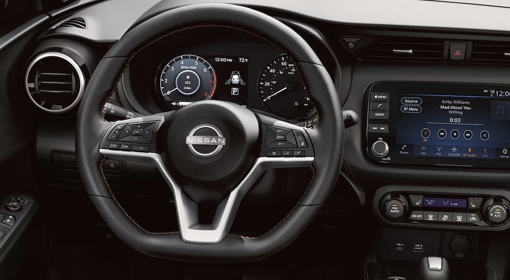 The black interior of a 2023 Nissan Kicks shows the steering wheel and infotainment screen.