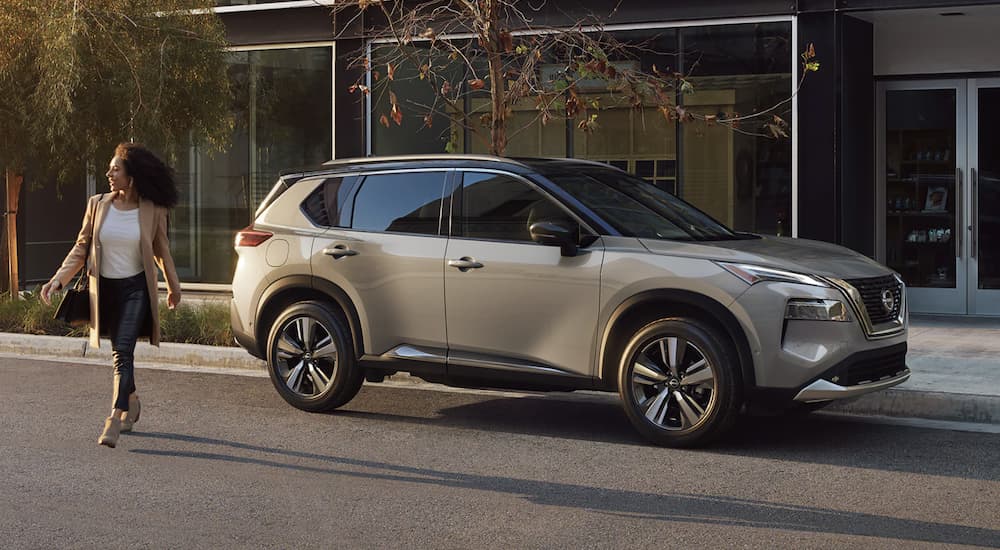 A grey 2023 Nissan Rogue is shown from the side parked in front of a building.
