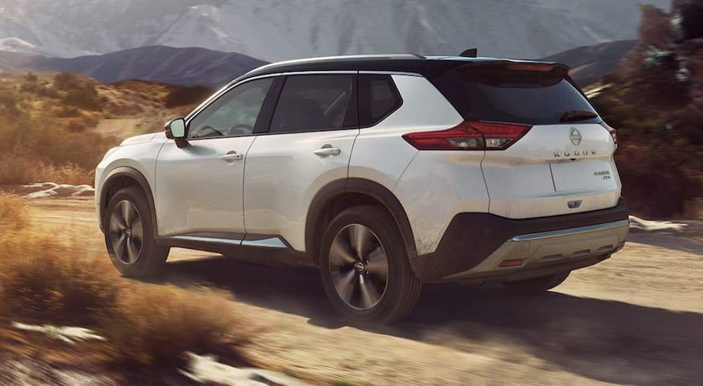 A white 2023 Nissan Rogue is shown from the rear driving on a dirt road.