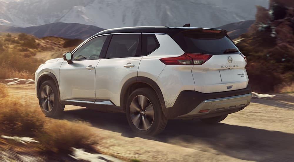 A white Nissan Rogue for sale near you, a 2023 Nissan Rogue, is shown driving on a dirt road.