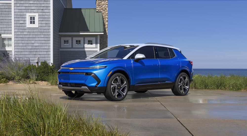 A blue 2024 Chevy Equinox EV is shown from the front at an angle near a coastal home after leaving a Chevy Equinox dealership.