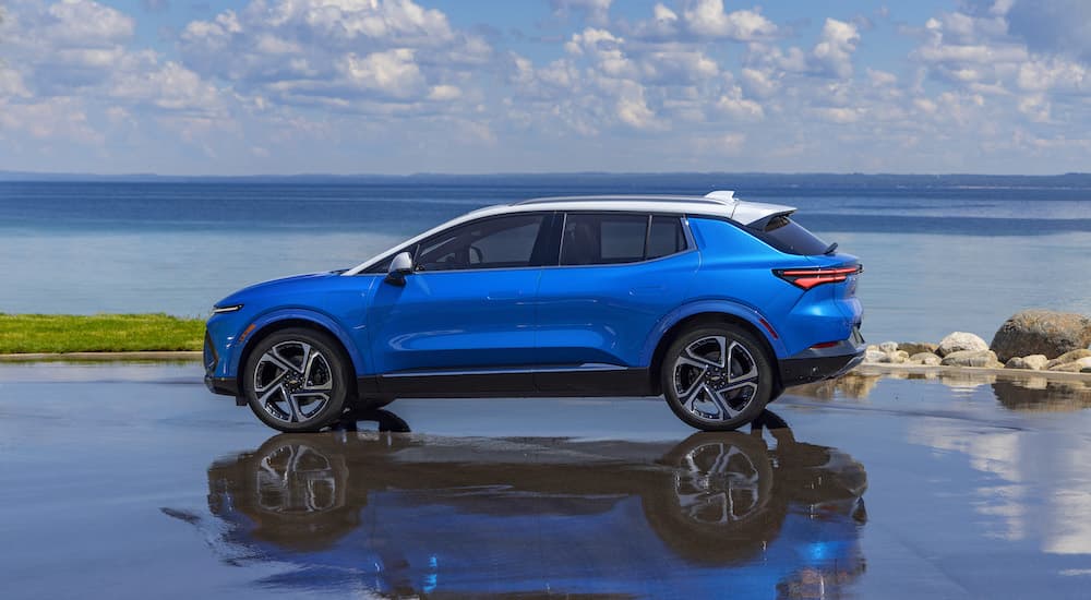 A blue 2024 Chevy Equinox EV is shown from the side while parked on a coast.