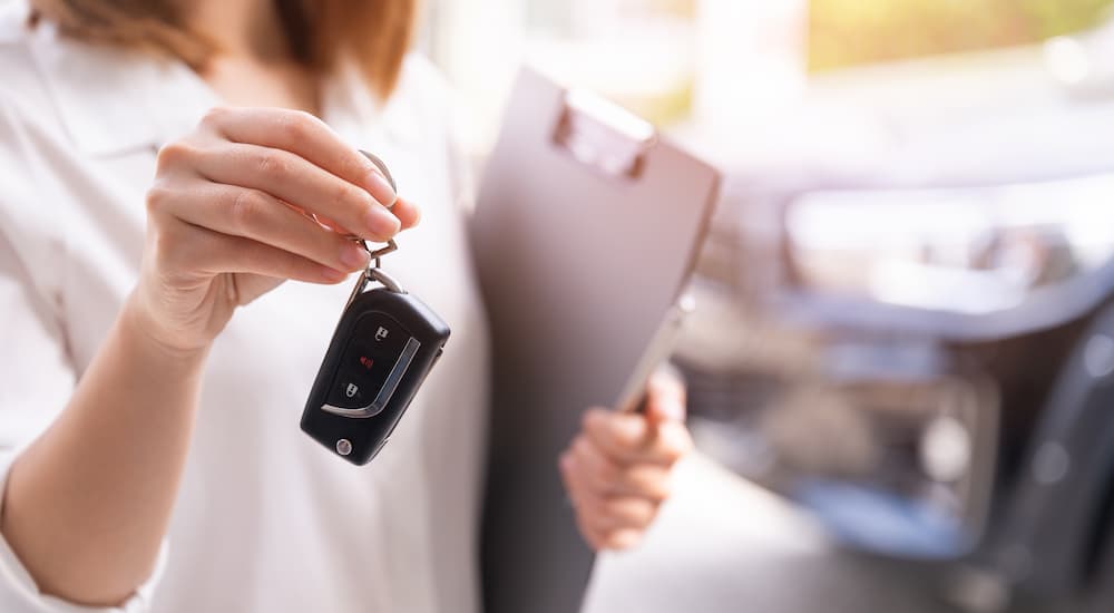 A saleswoman is shown holding a car key at a dealership.