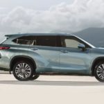 A person in a suit is shown walking next to a light blue 2021 Toyota Highlander Platinum.