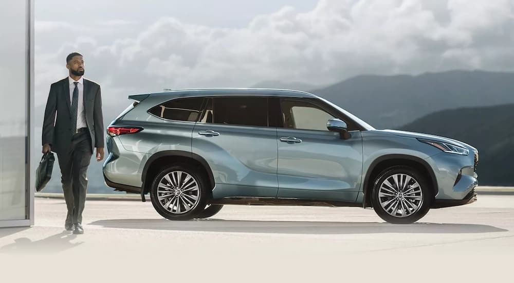 A person in a suit is shown walking next to a light blue 2021 Toyota Highlander Platinum.