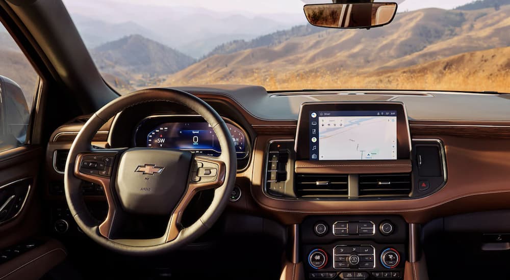 The brown interior of a 2023 Chevy Tahoe shows the steering wheel and infotainment screen.