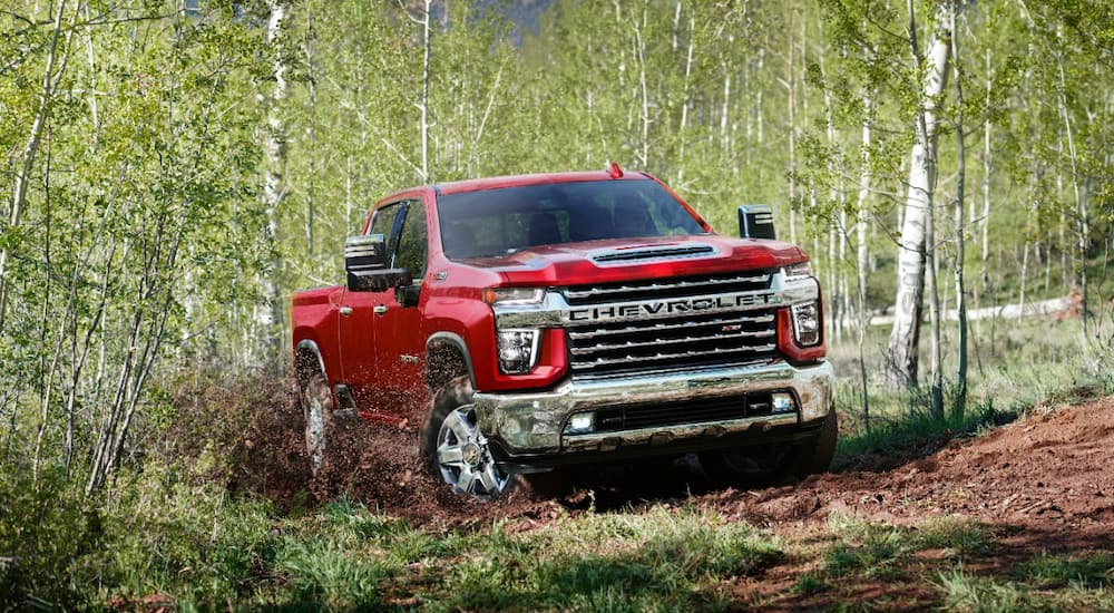 A red 2022 Chevy Silverado 2500HD is shown off-roading on a forest trail.
