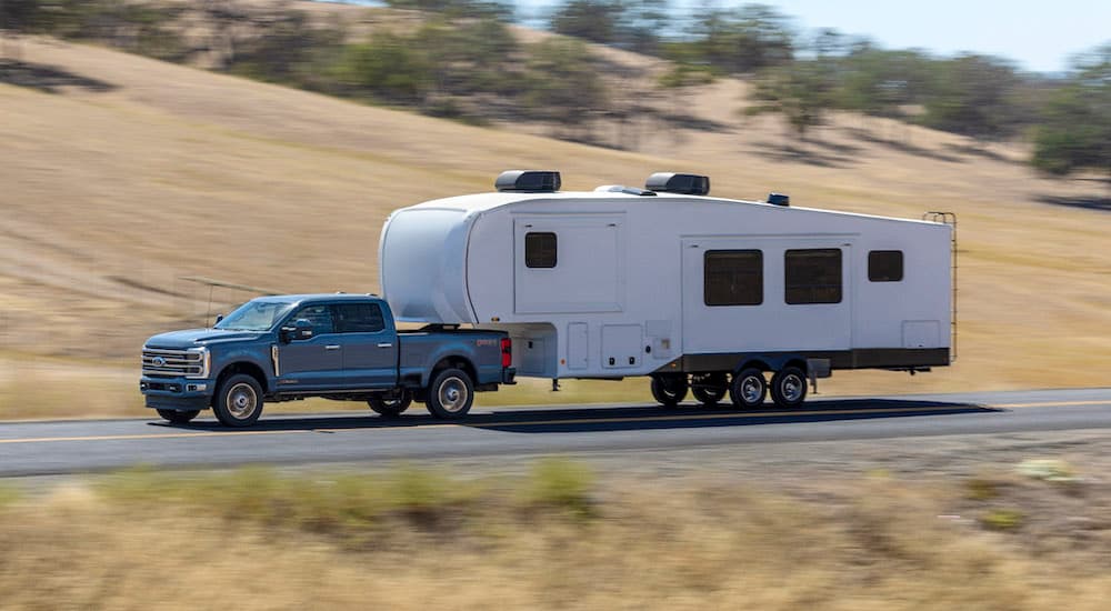 A grey 2023 Ford F-350 Super Duty is shown from the side while towing a camper.