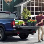 A man is shown putting plants into the bed of a blue 2022 Honda Ridgeline after visiting a Honda dealer.