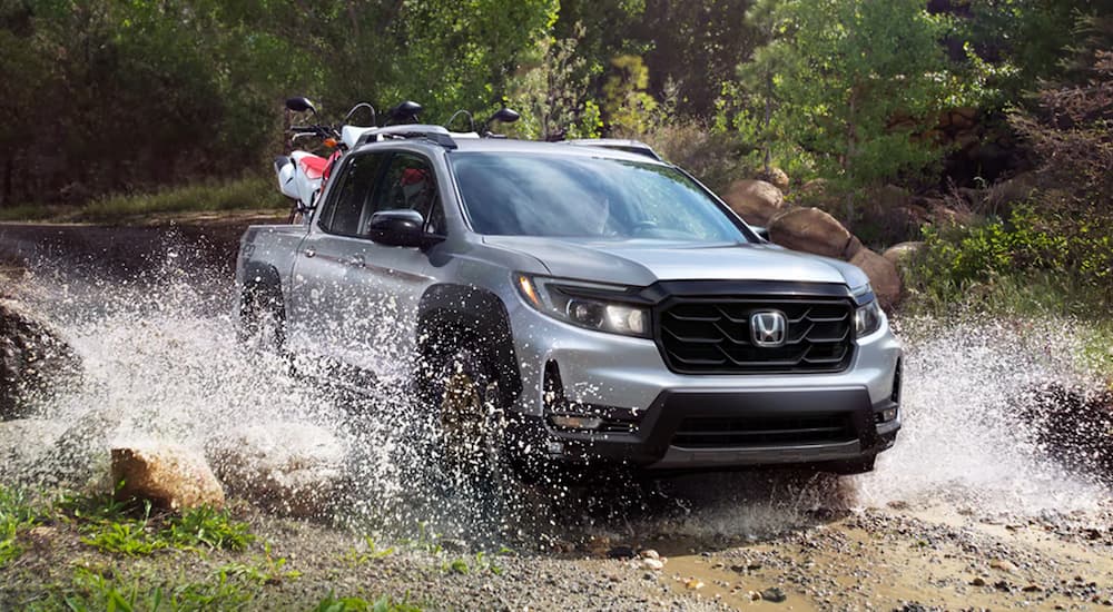 A silver 2022 Honda Ridgeline Sport is shown off-roading through a stream.