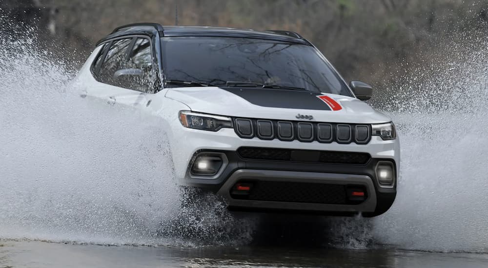 A white 2022 Jeep Compass Trailhawk is shown driving through a puddle.