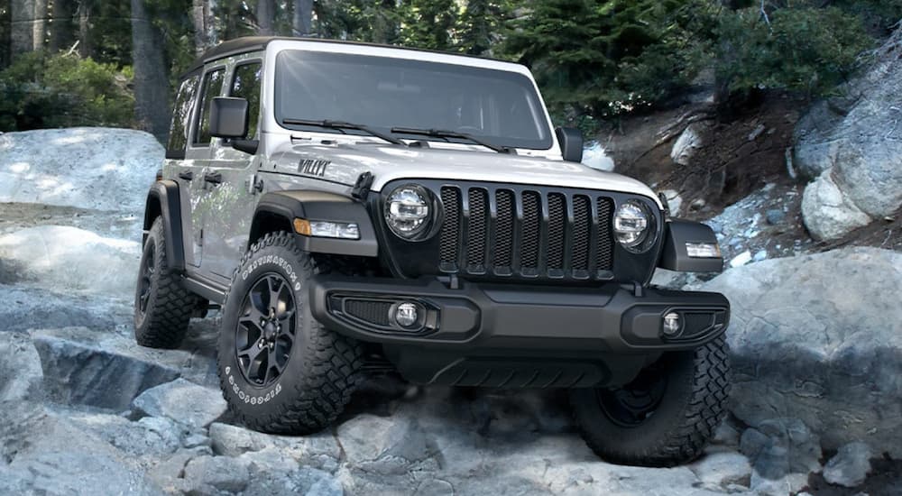 A silver 2020 Jeep Wrangler Willys is shown from the front while driving in a rocky area after leaving a used Jeep dealer.