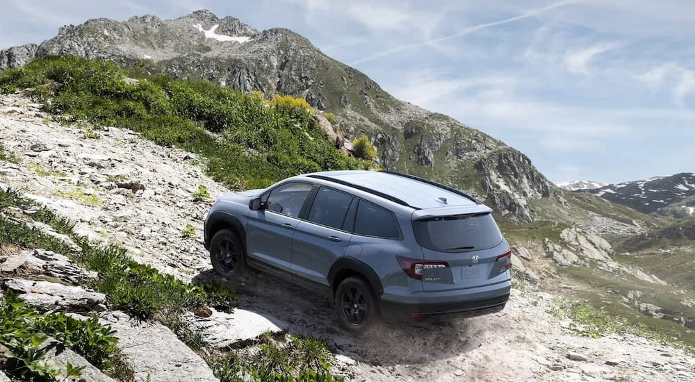 A grey 2022 Honda Pilot Trailsport is shown from the rear while going up a rocky trail.