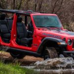 A red 2023 Jeep Wrangler 4xe is shown from the front at an angle while crossing a creek.