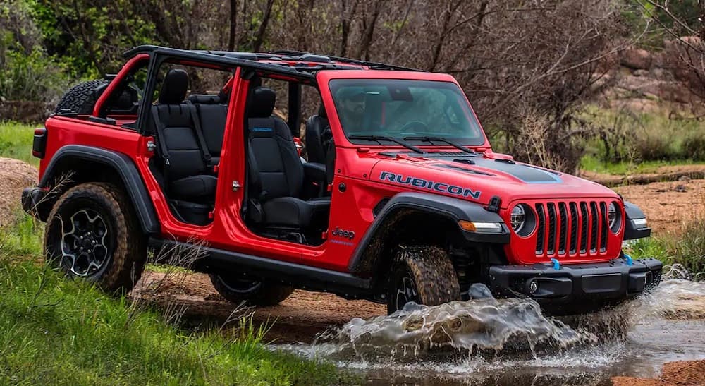 A red 2023 Jeep Wrangler 4xe is shown from the front at an angle while crossing a creek.