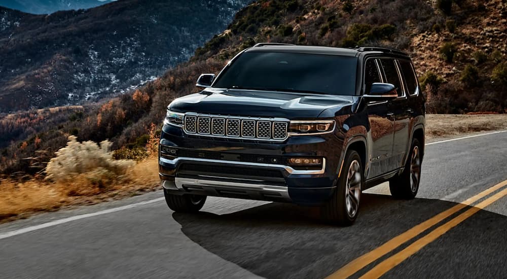 A black 2022 Grand Wagoneer is shown driving on an open road through the mountains.