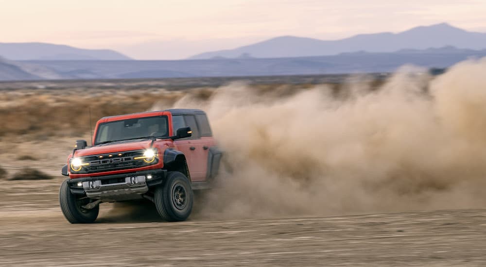 An orange 2022 Ford Bronco Raptor is shown sideways kicking up dust off-road.