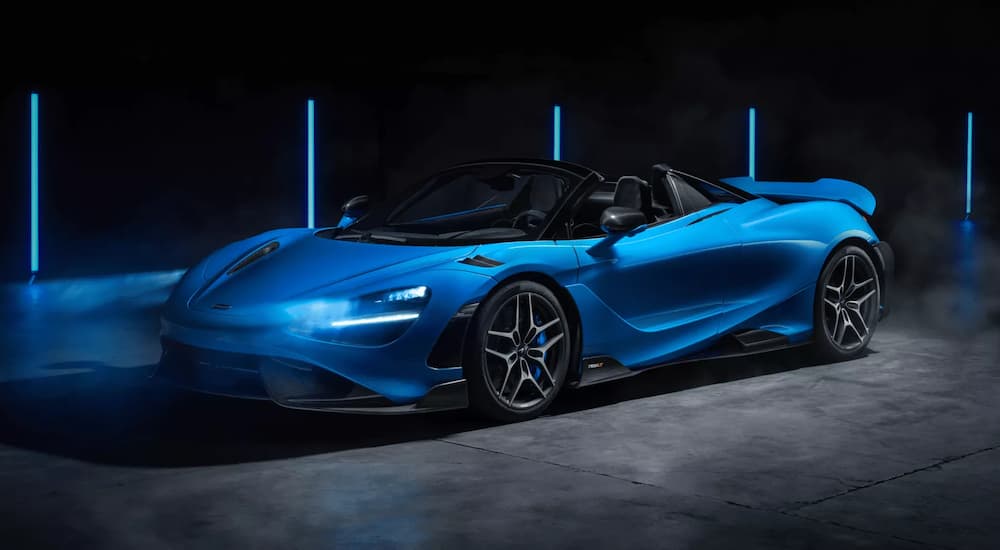 A blue 2022 McLaren 765LT Spider is shown parked in a modern gallery.