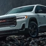 A white 2021 GMC Acadia AT4 is shown parked on rocks near the ocean.