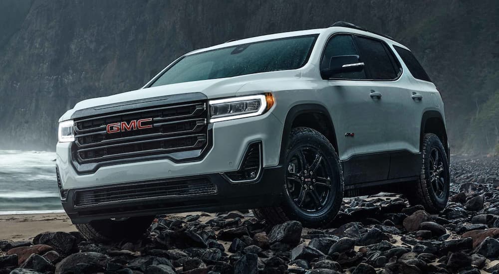 A white 2021 GMC Acadia AT4 is shown parked on rocks near the ocean.