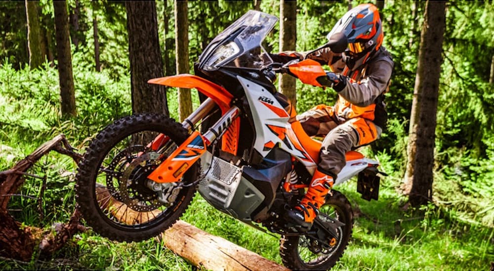 An orange 2022 KTM 890 Adventure R is shown from the side while jumping over a log.