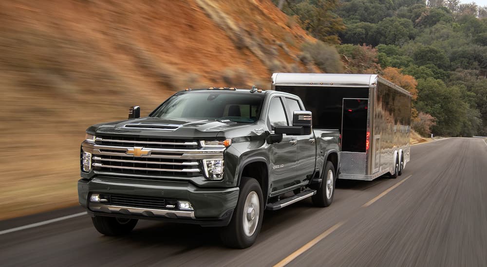 A black 2022 Chevy Silverado 2500HD is shown towing a black trailer on an open road.