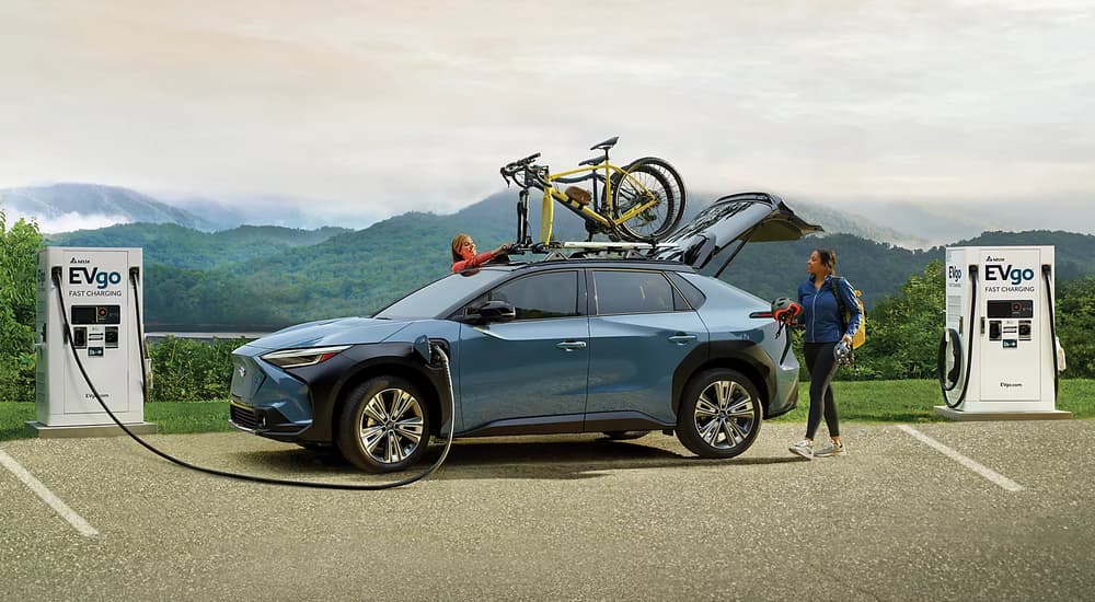 A blue 2023 Subaru Solterra is shown from the side while parked at an EV charging station.