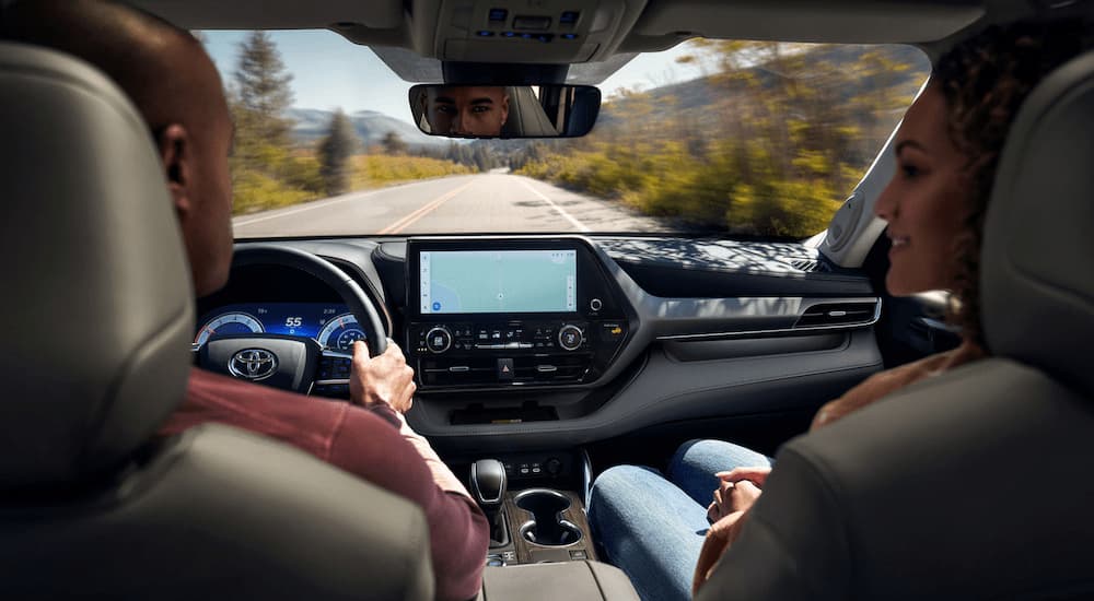 A couple is shown driving a 2023 Toyota Highlander on an open road.