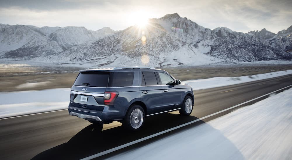 A blue 2018 Ford Expedition is shown driving past snow covered mountains after looking at used SUVs for sale.