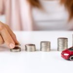 A person is shown creating stacks of coins in front of a toy car.