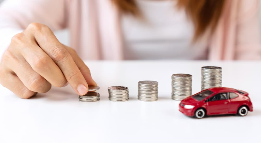 A person is shown creating stacks of coins in front of a toy car.