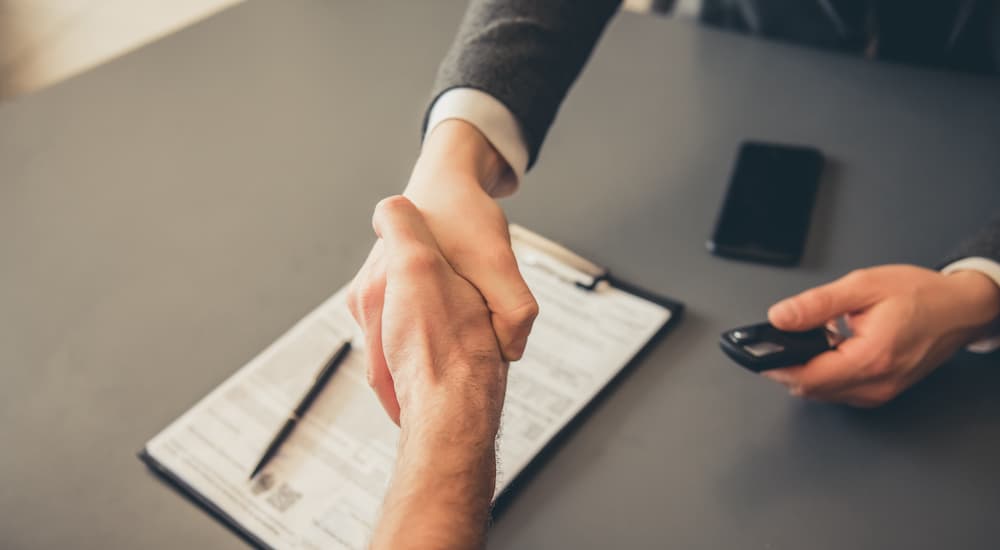 A salesperson is shown shaking hands over car loan paperwork after someone searched 'value my trade'.