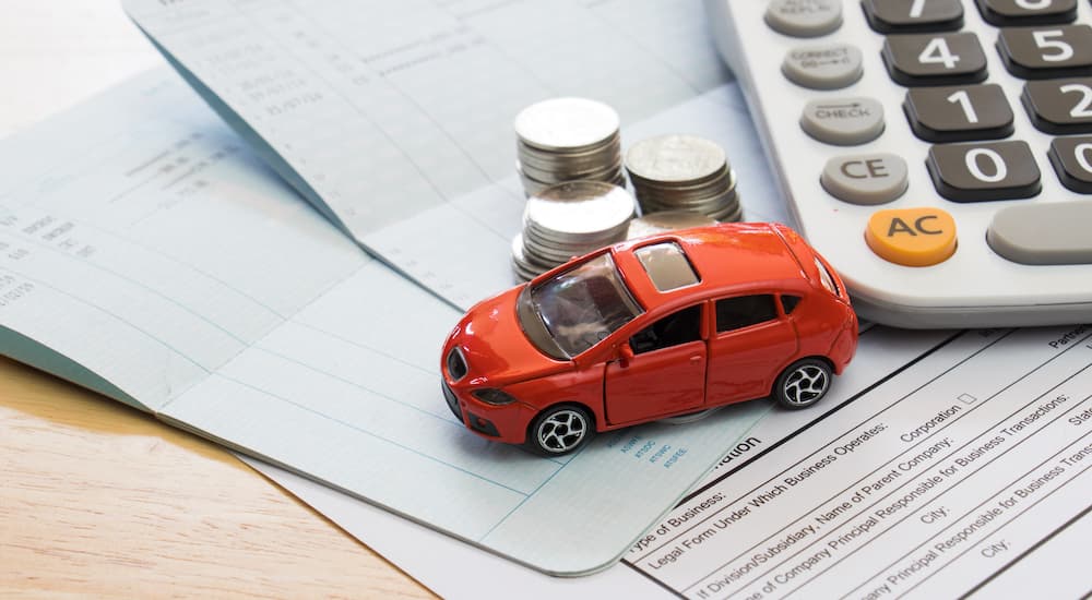 A toy car, coins, and a calculator are shown on top of paperwork.