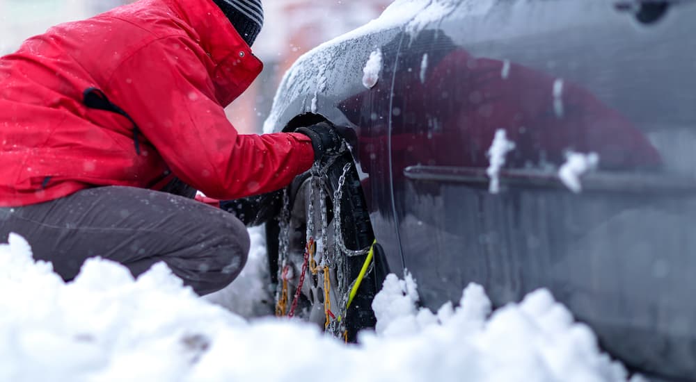 A person in a red coat is shown installing snow chains.