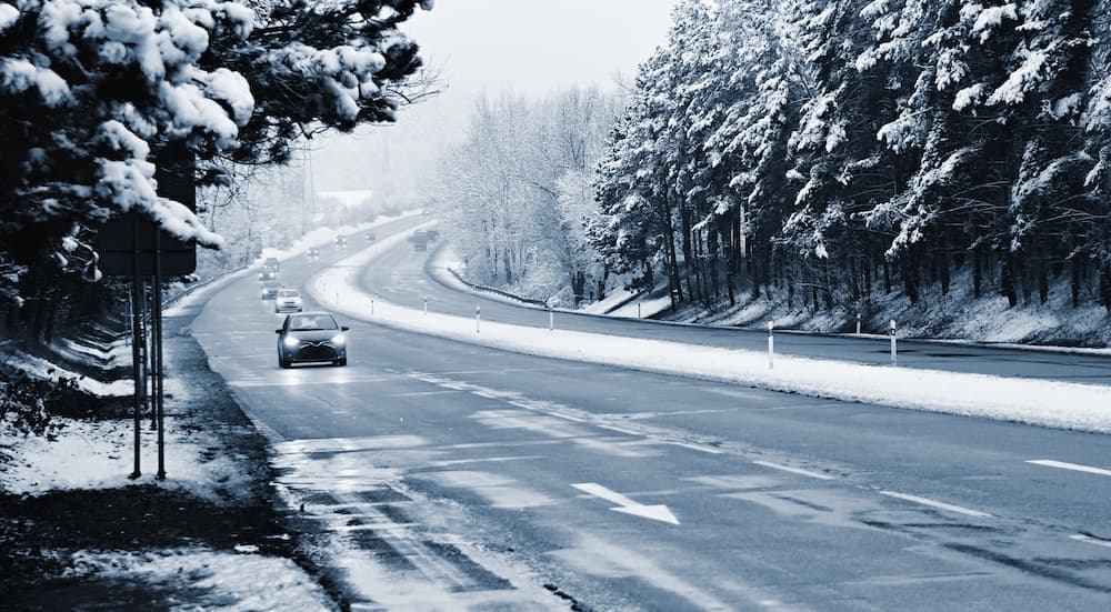 A close up shows a car driving on a snowy highway.