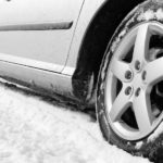 A close up of the side of a car driving on a snow covered is shown.