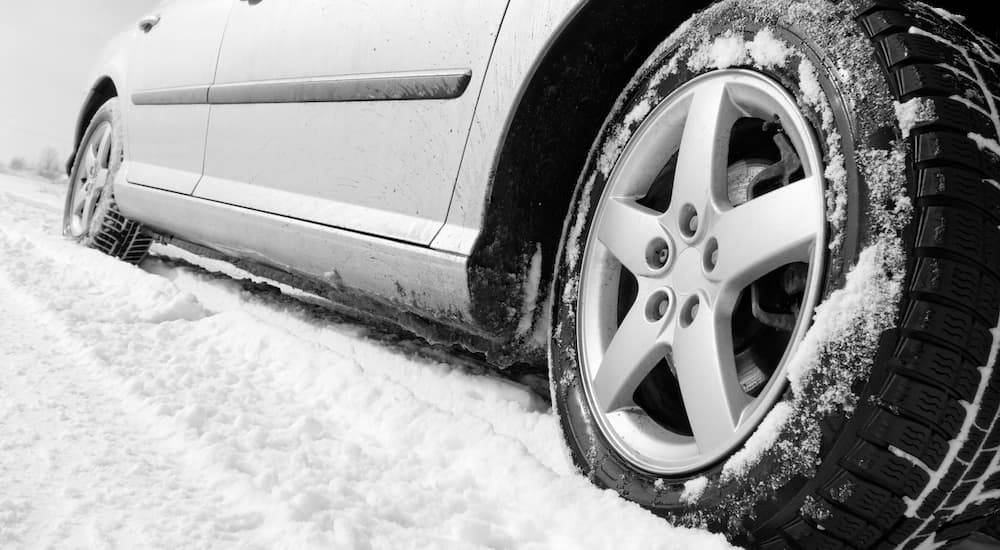 A close up of the side of a car driving on a snow covered is shown.