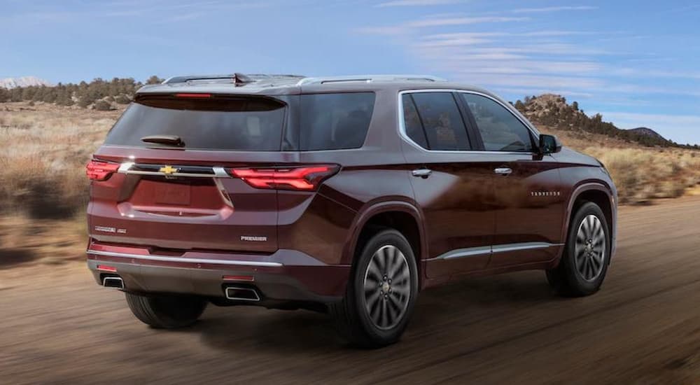 A maroon 2022 Chevy Traverse is shown from the rear driving on an open road.
