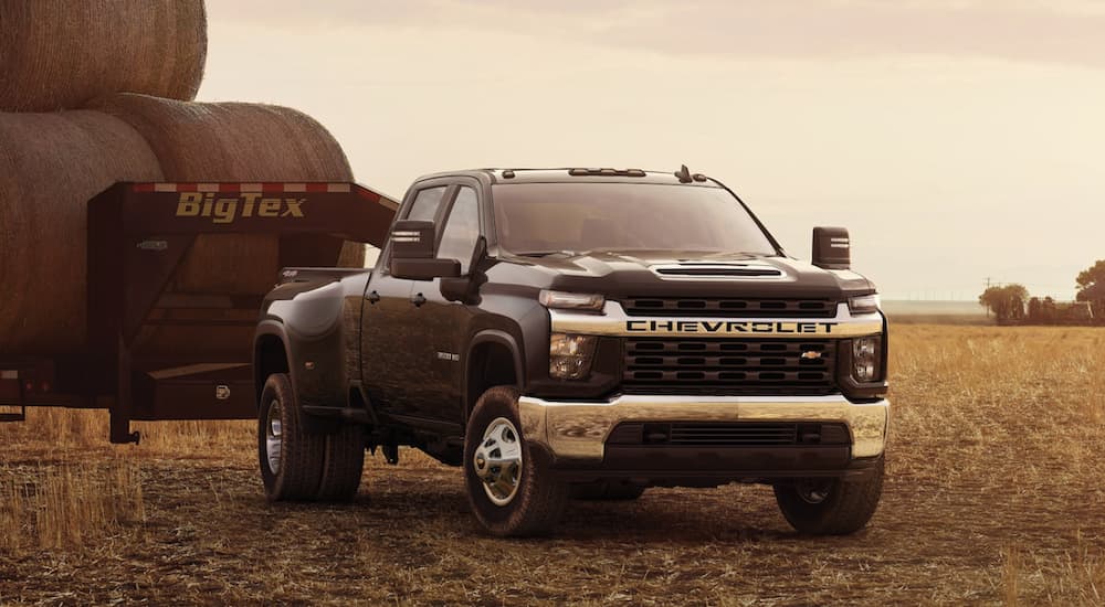 A black 2022 Chevy Silverado 3500 HD is shown parked in a field towing a trailer filled with hay.