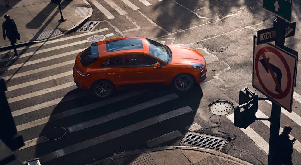 An orange 2022 Porsche Macan is shown from a high angle while driving through an intersection.