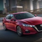 A red 2021 Nissan Altima is shown driving on a city street after leaving a used Nissan dealer.